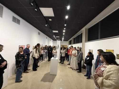 Photo of gallery space with black ceiling, white walls, and people lined up along both walls looking speaker.