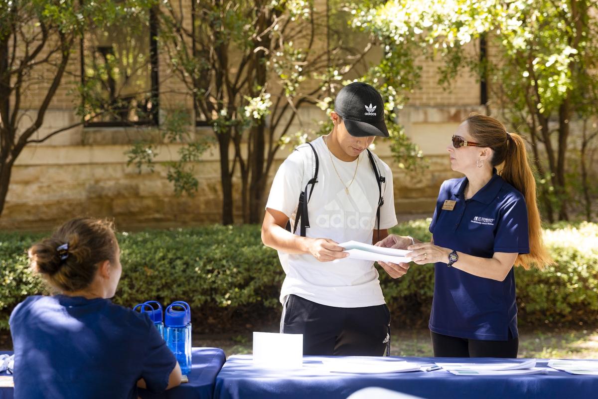 A woman and young man stand outside and look down at a paper.