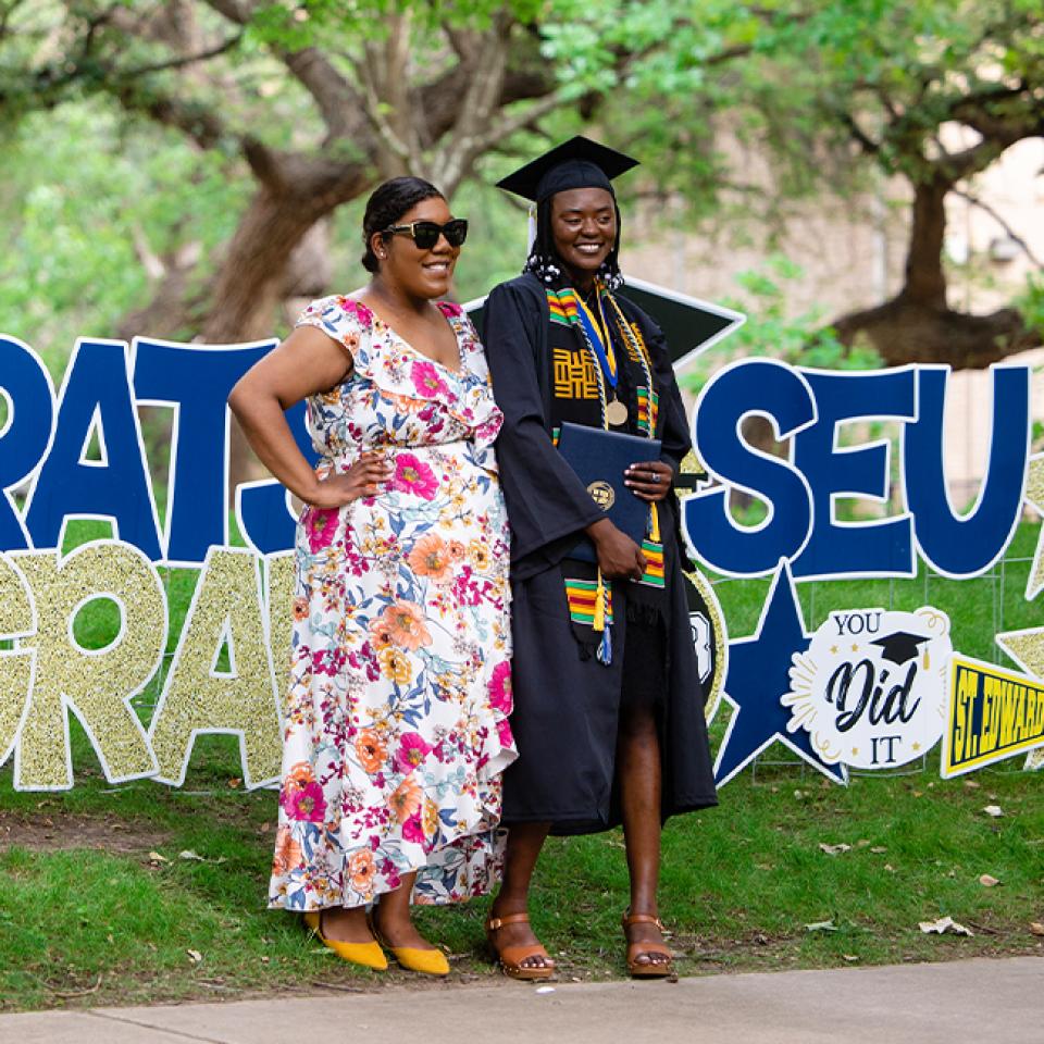 Graduate posing near celebration signs at Spring Commencement 2023