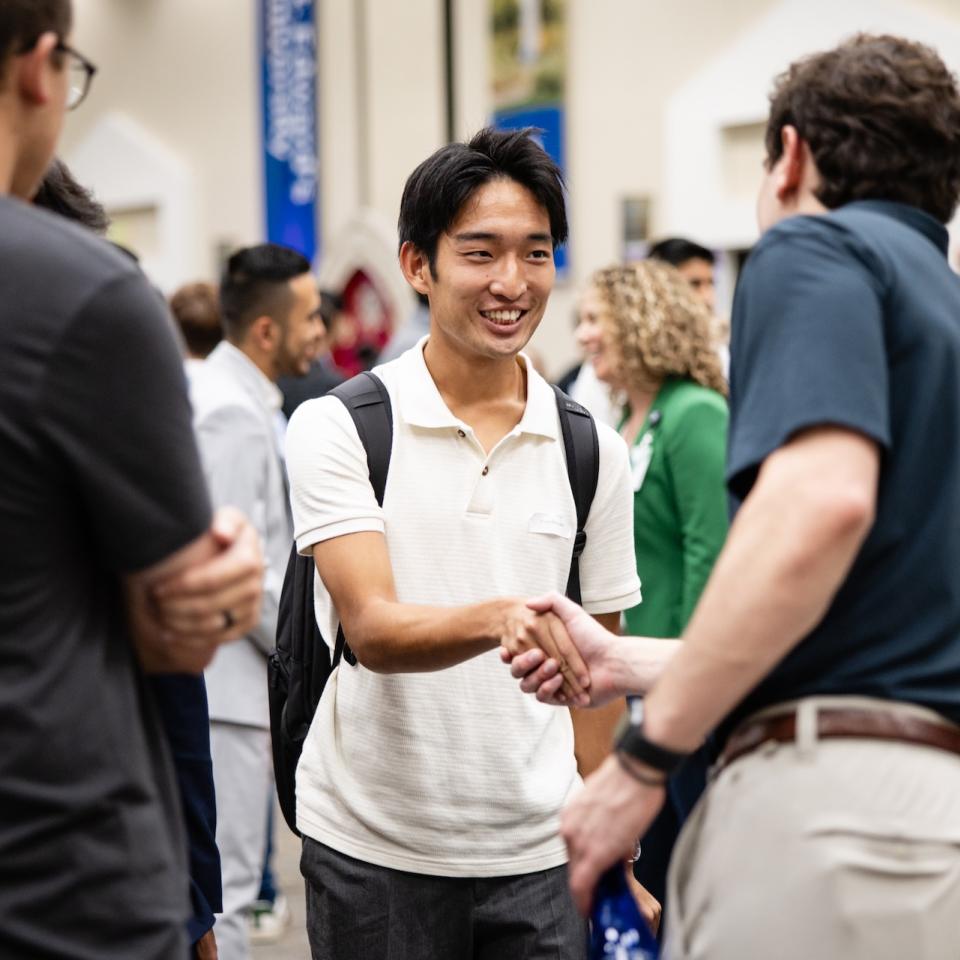 Two men shake hands while networking at a recruiting event.