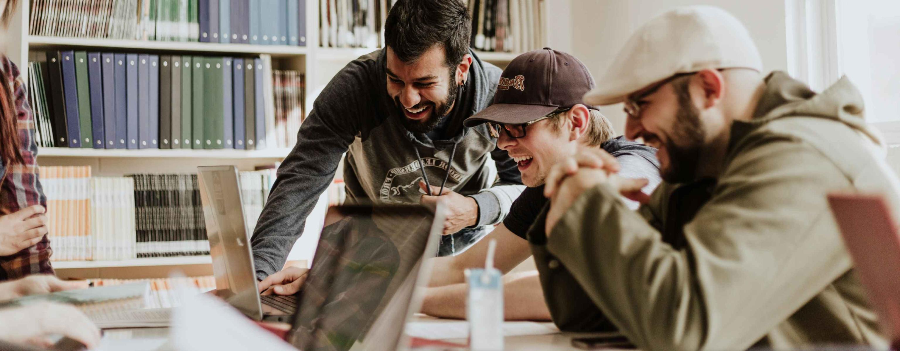 Three people working from one laptop smiling.