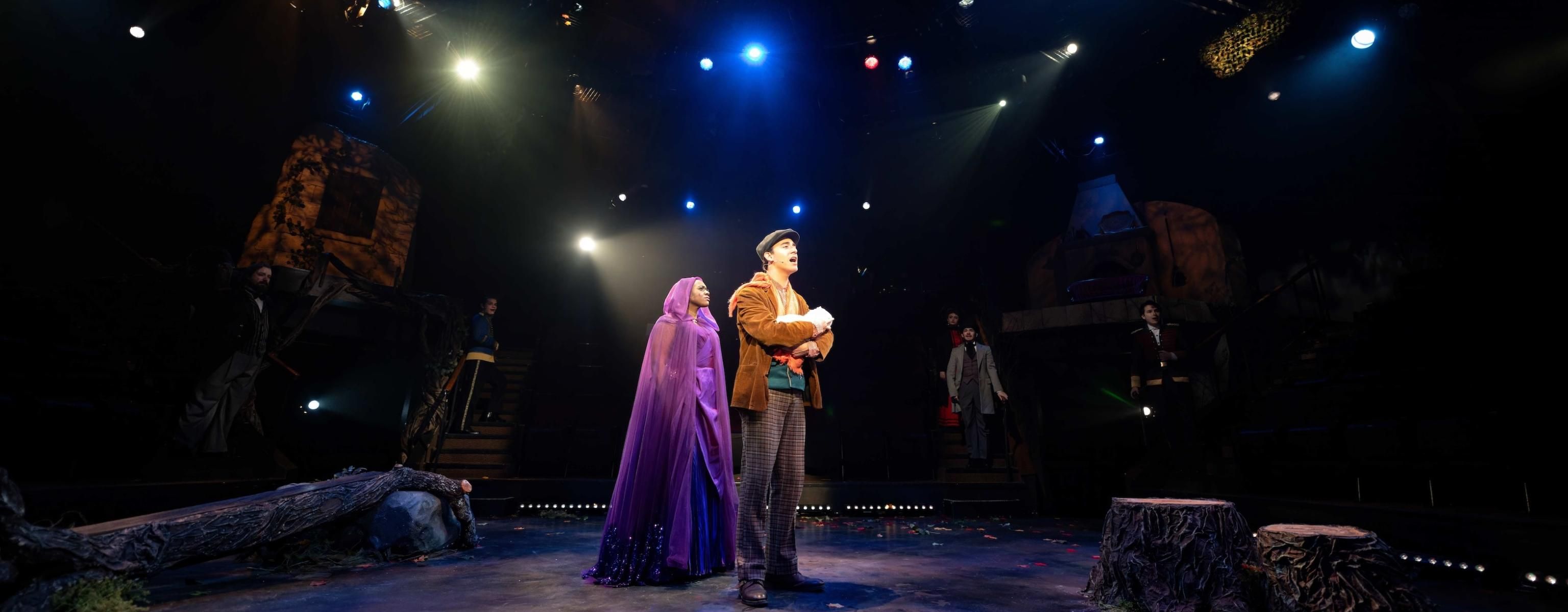 Actors in Into the Woods. They are playing the role of the Witch and the Baker. The Baker is holding a baby.