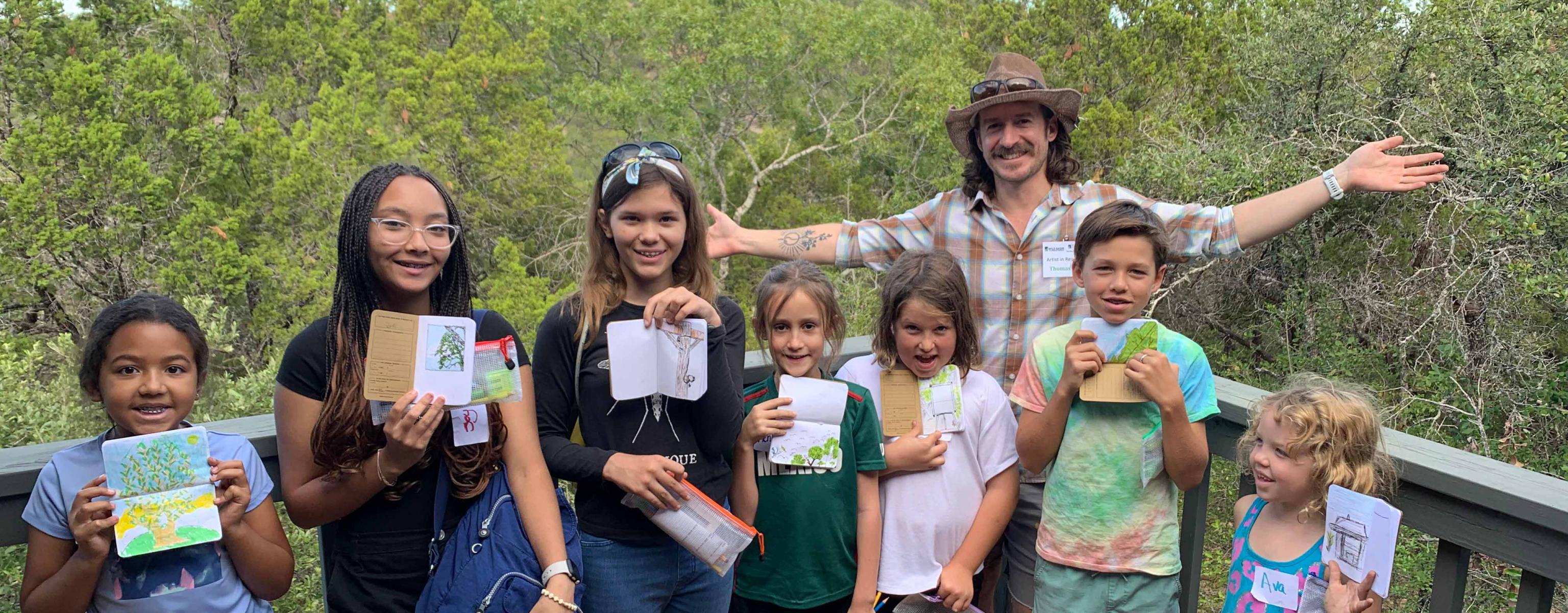 7 children and an adult posing in front of trees, all holding field guides
