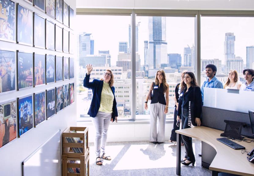 A woman stands in front of students at a SXSW office with downtown Austin showing in the background