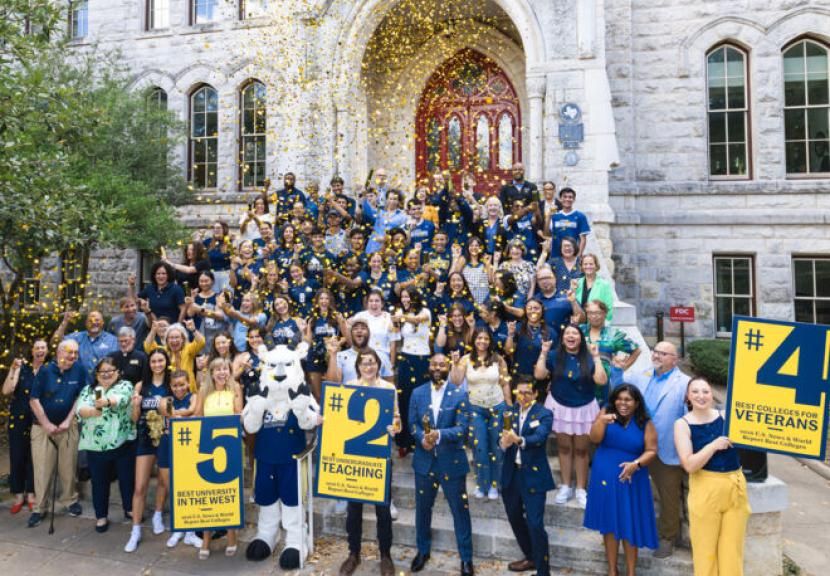A large, diverse group of students, faculty, staff and the Topper goat mascot celebrate on the stone steps of historic Main building. Gold confetti fills the air as people cheer and hold signs displaying "U.S. News & World Report" rankings, including #2 for Best Undergraduate Teaching and #5 Best University in the West.