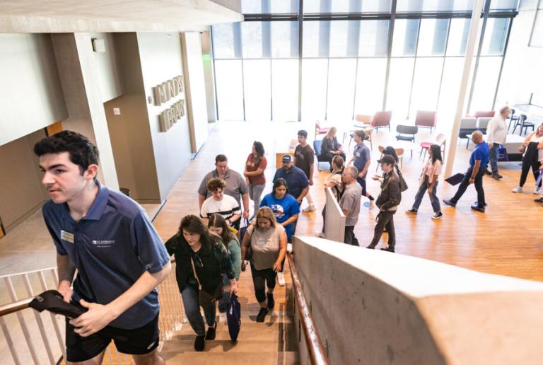 A student leading a campus tour group up the stairs of the library