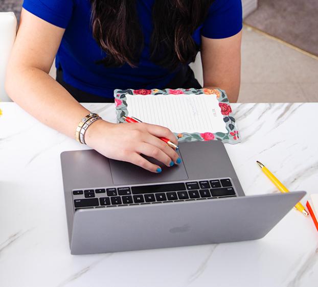 A woman at a desk using her laptop, with a vase of flowers nearby