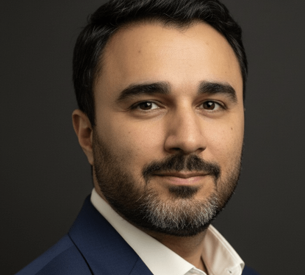 A headshot of a man with short, dark hair and facial hair