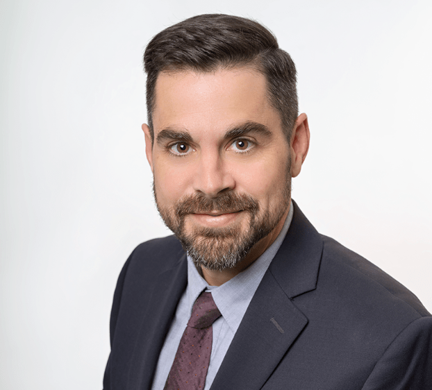 Professional headshot of a man in a navy blazer, light blue shirt, and maroon tie