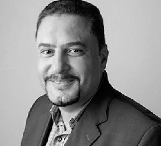 Professional headshot of a man in a suit jacket smiling against a neutral background