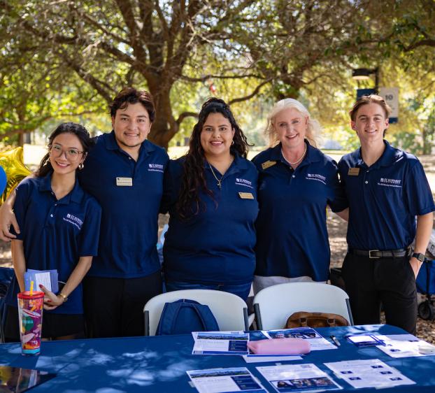 A group of college students smile for a photo outdoors with a faculty member.