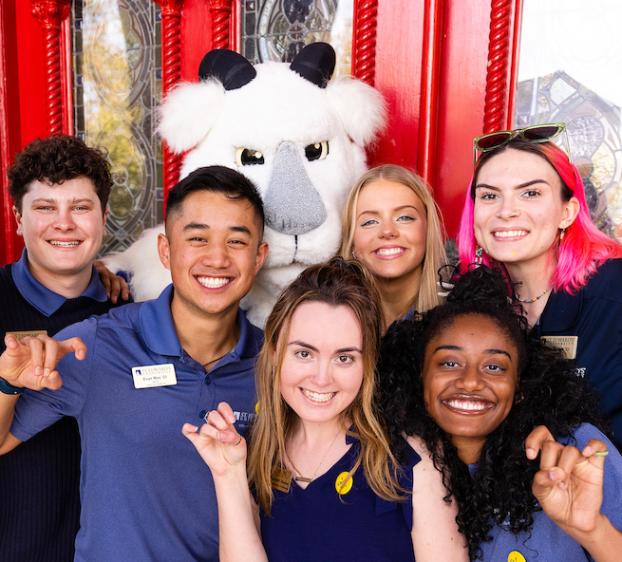 A group of students doing the "toppers up" with Topper in front of the Red Doors
