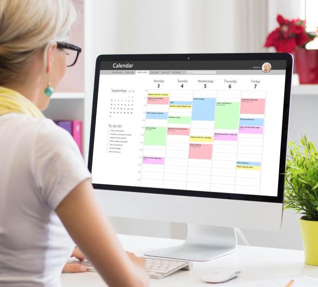 Blond woman with white shirt and yellow scarf looking at a calendar on her computer