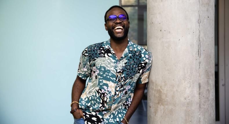 Schadrack Karekezi poses for a photo in front of a blue wall in the Natural Sciences building on campus