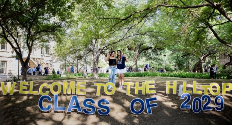 Two students pose in front of lawn signs that say "Welcome to the hilltop class of 2029"