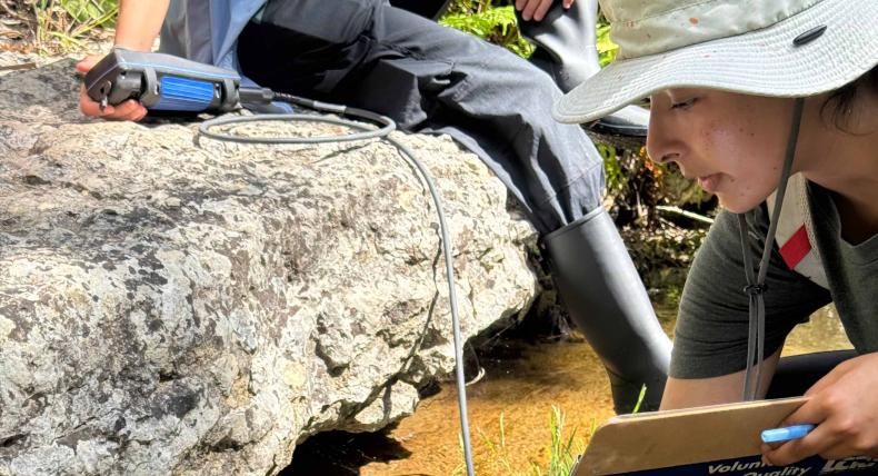 A woman by a creek holding a sensor wand underneath the water