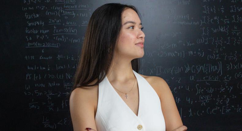 Student Chloe Roque poses in front of a Math Lab chalk board