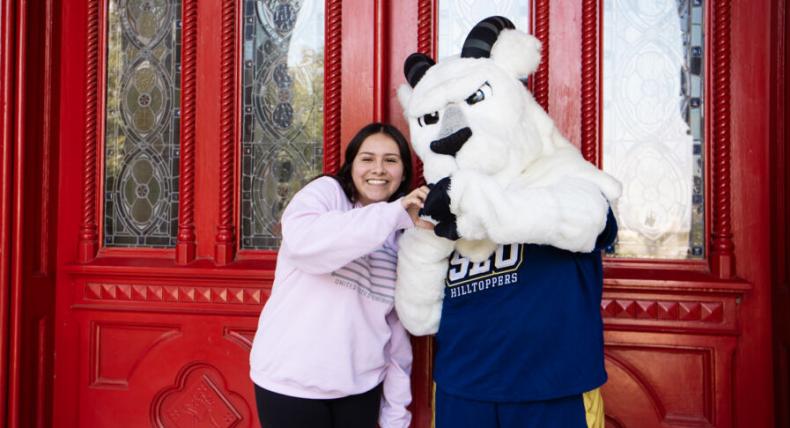 A student poses with the St. Edward's mascot Topper in front of the Main Building red doors for the First Day of School
