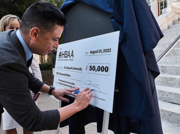 HBAA member and former university Trustee Jesse Butler sign a $50,000 donation check to St. Edward's University with president Montserrat Fuentes as witness