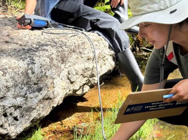 A woman by a creek holding a sensor wand underneath the water