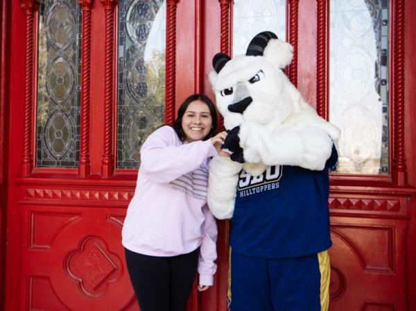 A student poses with the St. Edward's mascot Topper in front of the Main Building red doors for the First Day of School