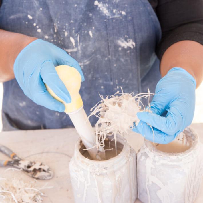 Tammie Rubin's hands hold a textured art piece as she adds porcelain slip to it.