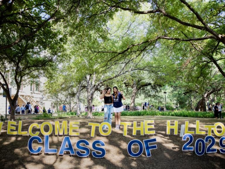 Two students pose in front of lawn signs that say "Welcome to the hilltop class of 2029"