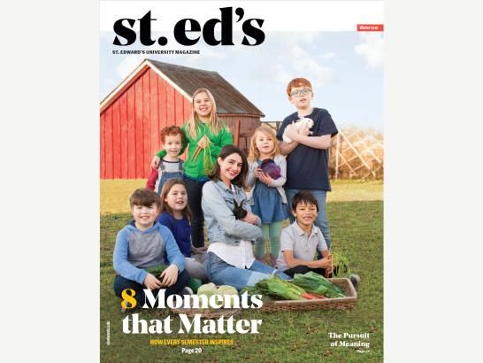 A mother and seven children sitting on a grassy field in front of a red barn