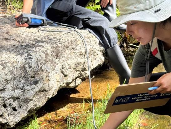 A woman by a river dipping a sensor want underneath the water