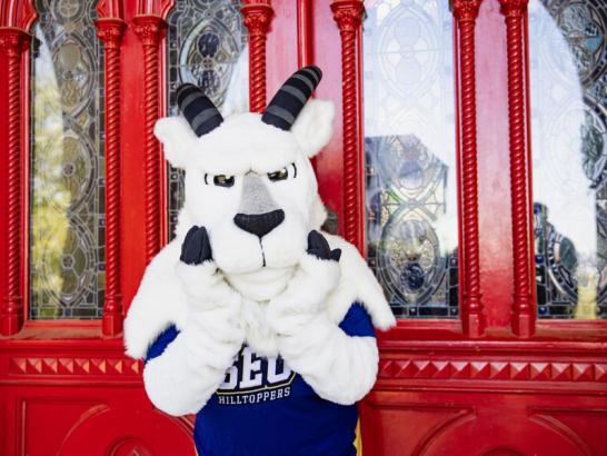 The Topper mascot stands in front of the Red Doors of Main Building holding his hooves up to his face