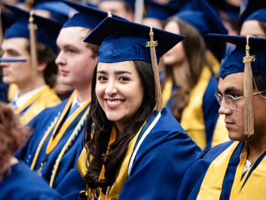A woman in a graduation cap and gown smiles with her fellow graduates