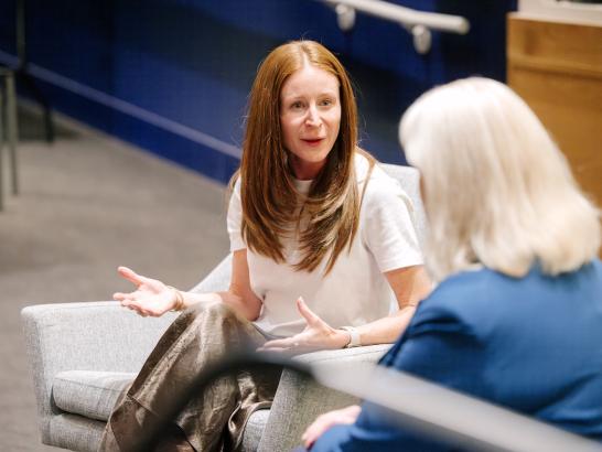 Two women talk to each other while sitting on a stage. 