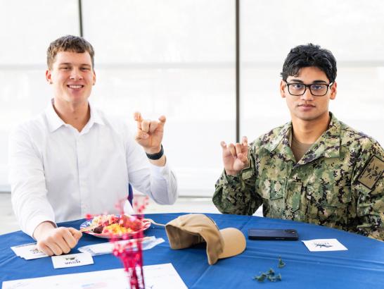 A man in a white shirt and a man in camouflage doing "Toppers up" with their hands