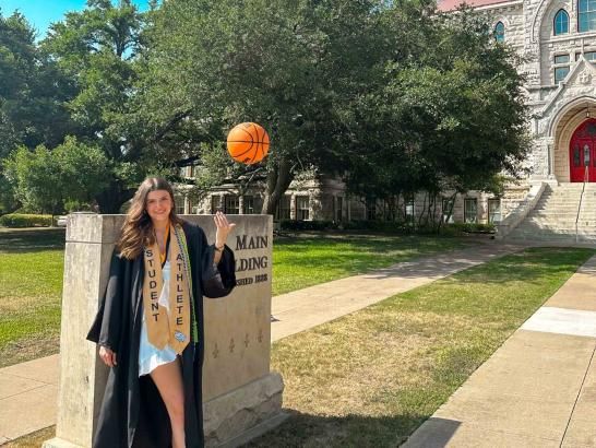 Alumna Matilda Soric' poses in her graduation gown in front of Main Building. 