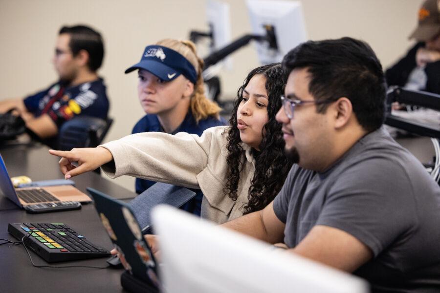 A group of three students look at a computer monitor one student is pointing to.