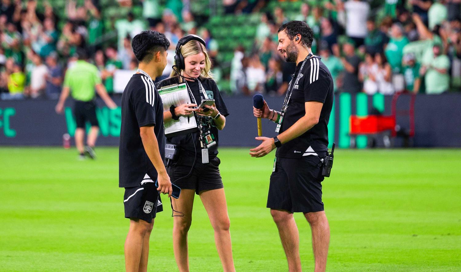 Alfredo Naim standing with other officials discussing on the field at Q2 stadium