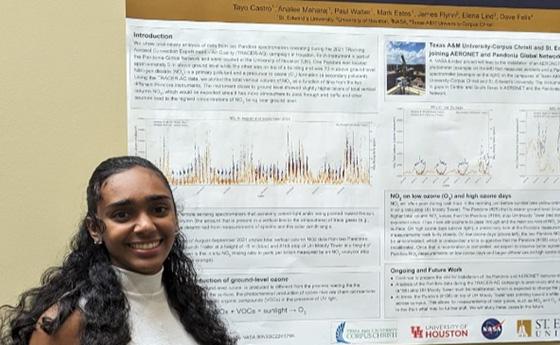 Analee Maharaj wears a white blouse and stands next to a poster board with her research.