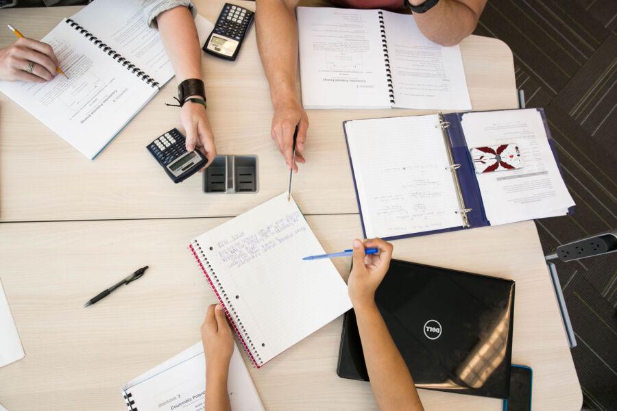 Aerial view of students gathering around a table in a classroom with notebooks