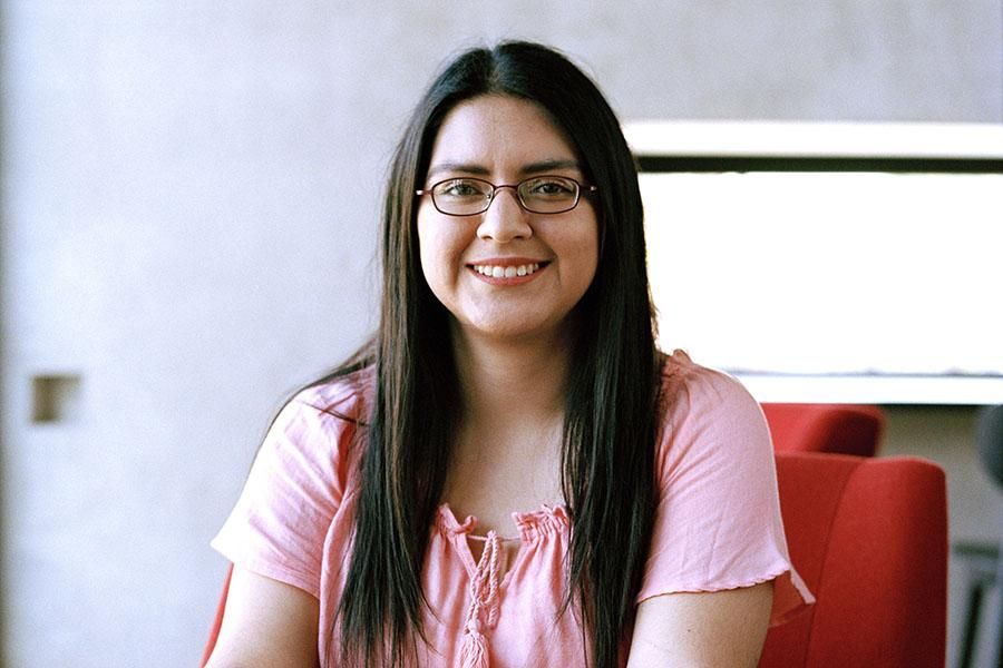 Sarahi Enriquez wears glasses and a pink blouse and sits in a red chair in the Munday Library.