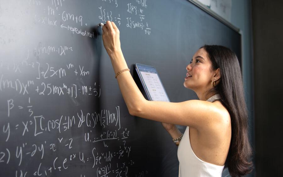 Student Chloe Roque poses in front of a Math Lab chalk board