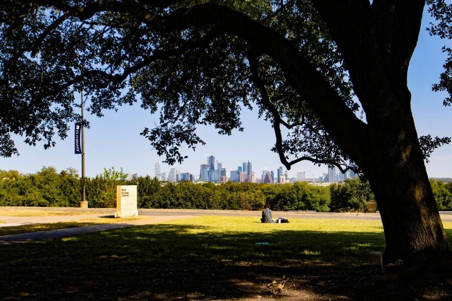 A student sits on the lawn of Main Building an enjoys the skyline views