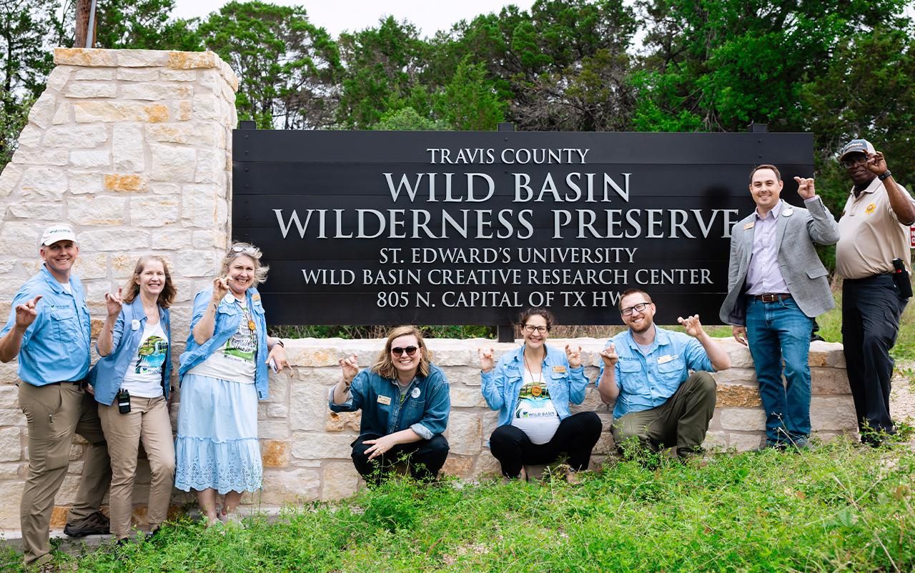 St. Edward's faculty and staff pose in front of the Wild Basin Wilderness Preserve signage.